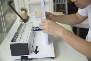 Man making report using comb binding machine - people working with stationary tools concept photo