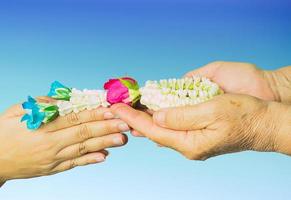 Young hands give jasmine garland to the older isolated over blue gradient background. Thai tradition for any special family occasions for paying high respective with love and care. photo