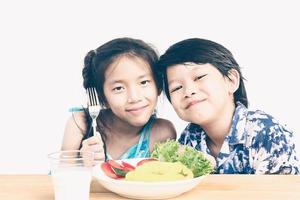 Vintage style photo of asian boy and girl are happily eating fresh vegetable salad with a glass of milk isolated over white background