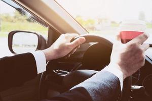 hombre conduciendo un auto mientras sostiene una taza de café foto