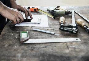 Carpenter working with wood furniture product preparation using  hand tools and machine table station while using mobile phone photo