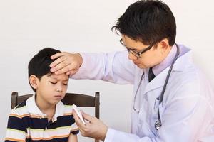 Sick Asian boy being examined by male doctor over white background photo
