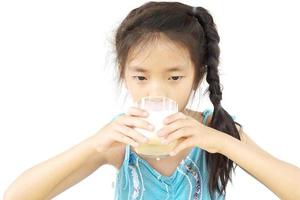 Chica asiática está bebiendo un vaso de leche sobre fondo blanco. foto