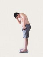 Soft focus of fat boy disappoint his fatness while standing on on weighing machine over white background photo