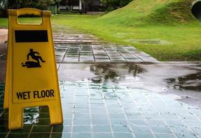 señal de precaución de suelo húmedo con gota de lluvia en el suelo de baldosas verdes foto