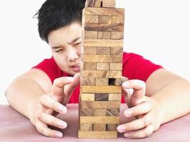 Asian kid is playing wood blocks tower game for practicing physical and mental skill. Photo is focused at model hands and isolated over white.