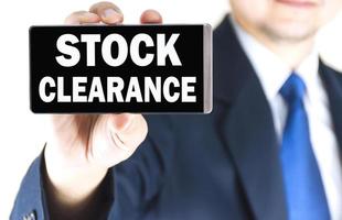 STOCK CLEARANCE word on mobile phone screen in blurred young businessman hand over white background, business concept photo