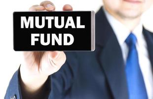 MUTUAL FUND word on mobile phone screen in blurred young businessman hand over white background, business concept photo