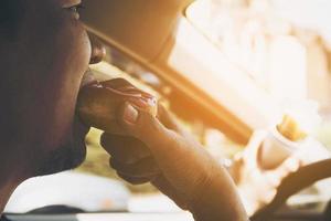 Man eating donuts and potato chip while driving car - multitasking unsafe driving concept photo