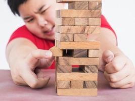 un niño asiático está jugando jenga, un juego de torre de bloques de madera para practicar habilidades físicas y mentales foto