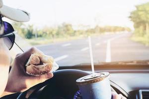 Man is dangerously eating hot dog and cold drink while driving a car photo