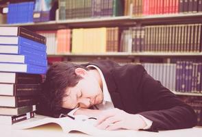 foto antigua de un hombre durmiendo mientras lee muchos libros en una biblioteca