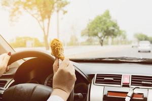 Business woman driving car while eating fried chicken dangerously photo