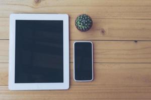 Vintage tone of top view of tablet and mobile on wooden table with small cactus photo