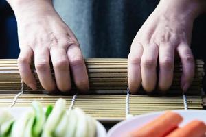 Chef preparando rollo de sushi sobre fondo de mesa negra - gente con plato favorito concepto de comida japonesa foto