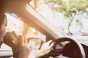 Lady driving car while eating hamburger photo