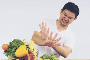 Vintage photo of Asian man showing dislike expression of fresh colorful vegetables isolated over white background