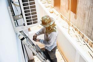 Man is installing wall compressor of air conditioner during hot season photo