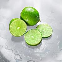 The green lime is blank with the cut lime slice showing the inside of the wet lemon pulp on a clear glass surface, reflecting the shadows of the lime and the wet water, giving it its freshness. photo