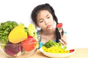 Una chica encantadora asiática que muestra una expresión aburrida con verduras frescas y coloridas aisladas sobre fondo blanco foto