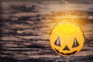 Dark tone photo with of Halloween pumpkin face with warm golden dot evaporate on top of bucket over old wooden texture