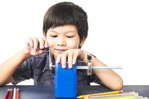 A boy is sharpening his pencil using mechanical sharpener over white background photo