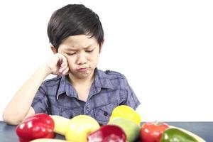 Asian boy is showing dislike vegetable expression over white background photo