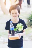 niño encantador asiático mostrando su caja de almuerzo en la escuela foto