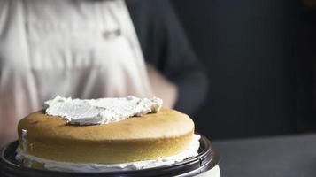 señora haciendo pastel poniendo crema con espátula - concepto de cocina de panadería casera foto