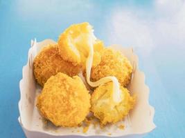 Sticky stretch cheese balls in paper container over blue table background photo