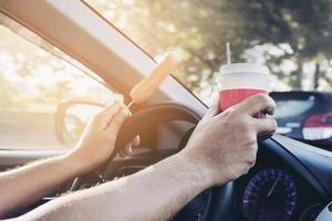 hombre conduciendo un auto mientras sostiene café y hotdog, comportamiento malo y peligroso foto