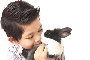 niño asiático jugando con un encantador conejo bebé aislado sobre blanco foto