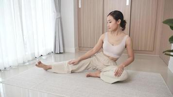Girl in sportswear doing stretching exercises while sitting on a mat at home. video