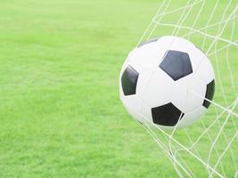 Shooting shot, football in goal net with green grass field background photo