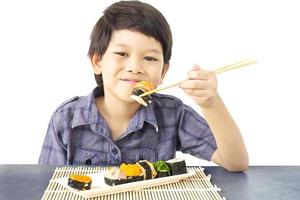 Chico encantador asiático está comiendo sushi aislado sobre fondo blanco. foto