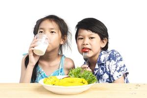 niño y niña asiáticos que muestran disfrutar de la expresión con verduras frescas y coloridas y un vaso de leche aislado sobre fondo blanco foto