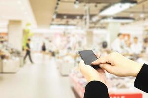 hombre que usa un teléfono móvil sobre un fondo de supermercado borroso foto