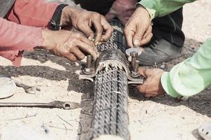 mano de obra hombre que trabaja con el perno del tendón de la eslinga del puente apretando el trabajo de construcción - personas en el concepto de trabajo de construcción del sitio foto