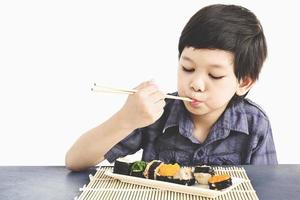 Chico encantador asiático está comiendo sushi sobre fondo blanco. foto