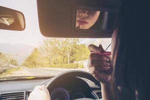 Woman making up her face using lipstick while driving car, unsafe behavior photo