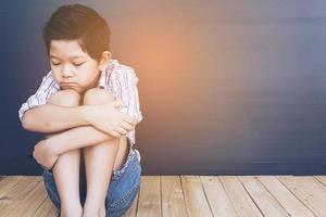 Sad Asian boy sitting on white wood floor photo