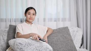 asiatische junge frau sieht fern und sitzt glücklich im wohnzimmer zu hause auf dem boden video