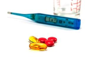 Fish oil and medicine pills with blurred thermometer and glass on white background photo