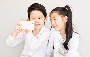 una encantadora pareja asiática de niños de la escuela se está tomando selfie, de 7 y 10 años, sobre fondo gris foto