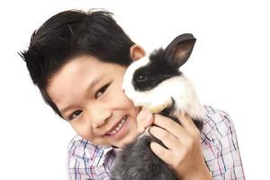 niño asiático jugando con un encantador conejo bebé aislado sobre blanco foto