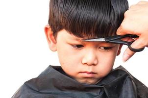 un peluquero le corta el pelo a un niño sobre fondo blanco, concéntrese en su ojo derecho foto