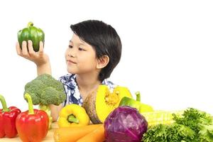 niño sano asiático que muestra una expresión feliz con una variedad de verduras frescas y coloridas sobre fondo blanco foto