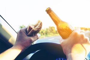 Man eating hotdog with beer while driving a car dangerously photo