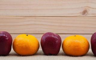 manzanas y naranjas frescas con gota de agua puesta sobre tela de saco sobre fondo de madera foto