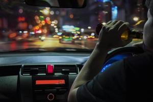 el hombre bebe cerveza mientras conduce de noche en la ciudad peligrosamente, sistema de conducción a la izquierda foto